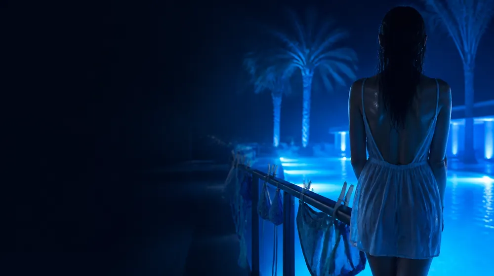Micro Bikini OnlyFans creators — woman at the edge of a glowing pool at night, a string bikini drying on the pool rail