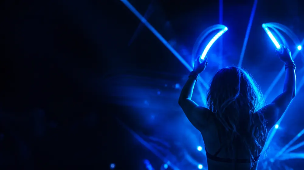 Rave Girl OnlyFans creators — woman dancing under sweeping laser beams, glowsticks arcing light trails around her