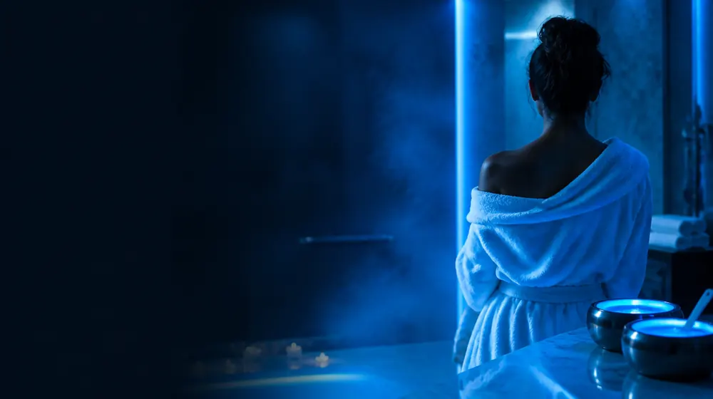 Waxing OnlyFans creators — woman wrapped in a towel in a steamy glowing spa, honey-toned wax pots warming on the counter